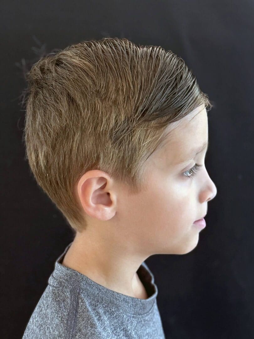 Profile of a young boy with a short haircut against a black background.