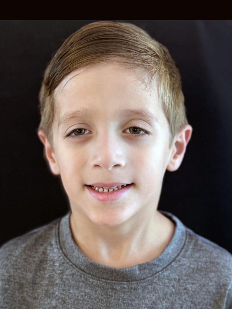Portrait of a young boy with light brown hair and a gray shirt.
